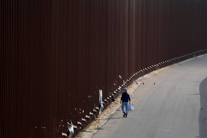 A volunteer walks along a border wall as she passes out baby wipes to migrants waiting to apply for asylum between two border walls Thursday, May 11, 2023, in San Diego. Many of the hundreds of migrants between the walls that separate Tijuana, Mexico, with San Diego have been waiting for days to apply for asylum. Pandemic-related U.S. asylum restrictions, known as Title 42, are to expire May 11. (AP Photo/Gregory Bull)