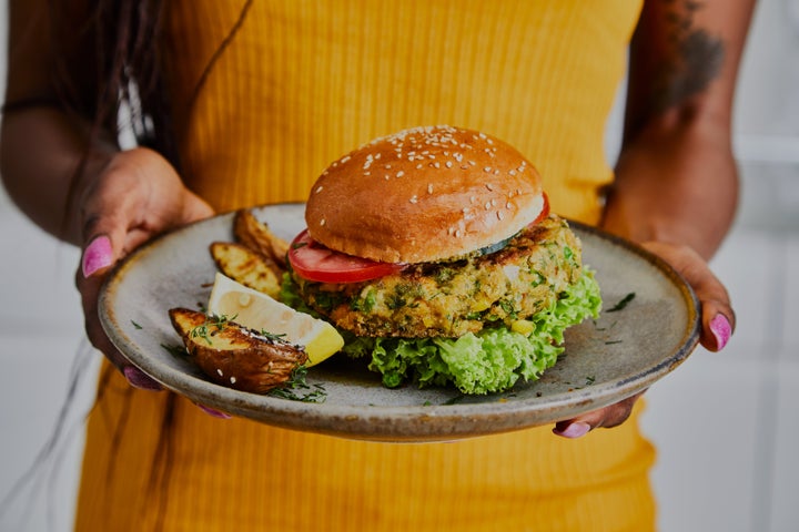 A woman holds a healthy vegan burger on a handmade ceramic plate, made of zucchini, green pea, seasoning, herbs and spices, close up