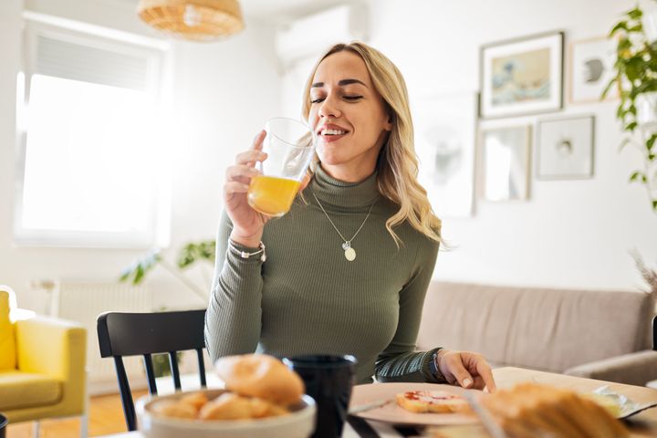 Young woman eating and drinking orange juice while sitting at home