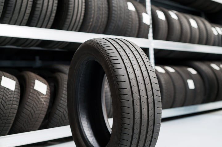 Fresh new black tire of car on floor near stack counter with tires in modern shop