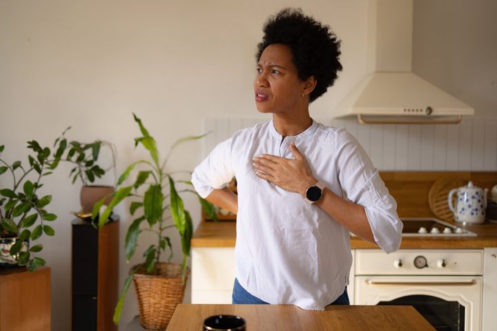 Displeased African American woman feeling pain in her chest in the kitchen.