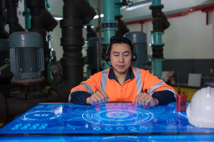 Asian Male engineer working at Illuminated table display with futuristic smart function for finding solution in the machine room.