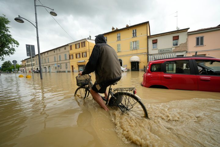 A cyclist rides through a flooded street in the village of Castel Bolognese, Italy, Wednesday, May 17, 2023.