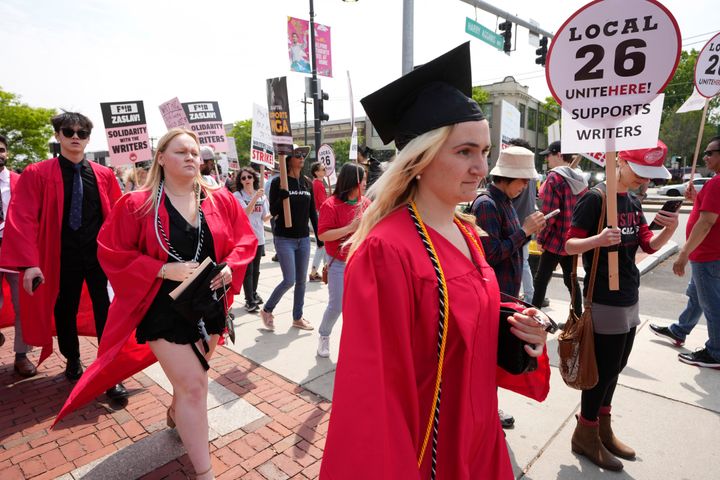 Graduates walk past protesters supporting the writers' strike outside an entrance to Boston University commencement ceremonies on Sunday.