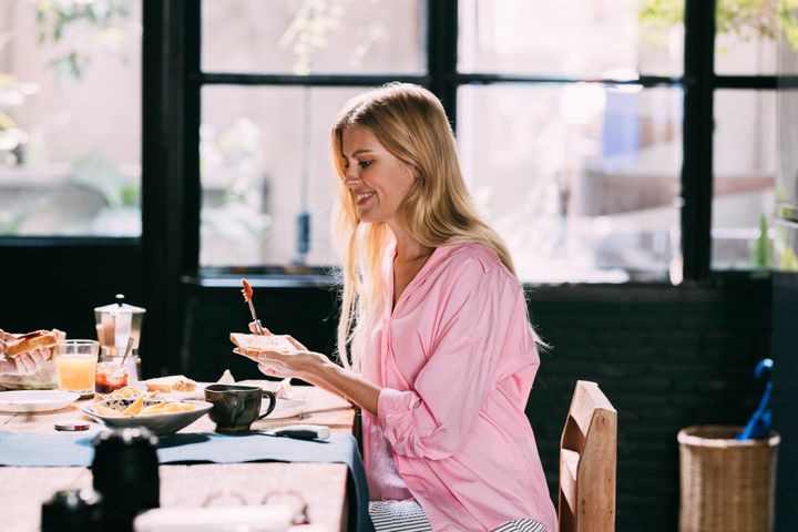 A side view of a smiling Caucasian female sitting at the table and having a healthy meal.