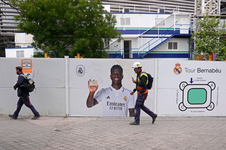 Workers pass a poster of Real Madrid's Vinicius Junior outside the Santiago Bernabeu stadium in Madrid, Spain, Monday, May 22, 2023. Spanish soccer is again embroiled in a racism debate after yet another case of abuse against Real Madrid forward Vinicius Junior, with the president of Spain's soccer federation acknowledging that the country has a racism problem and the player's club asking authorities to investigate the latest incident as a hate crime. (AP Photo/Paul White)