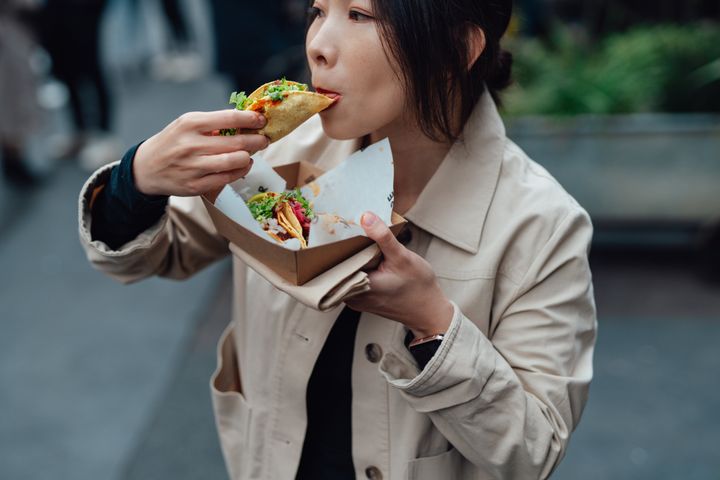 A young Asian woman is taking a lunch break and enjoying some Mexican tacos in an outdoor street food market. Street food concept.