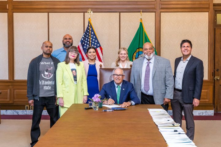 David Heppard (left), the executive director of the Freedom Project, attends the bill signing ceremony with Gov. Jay Inslee earlier this month while wearing a shirt that reads, "What if the 13th amendment wasn't retroactive?" Chelsea Moore, the Look2Justice co-founder, stands to the right of Heppard.