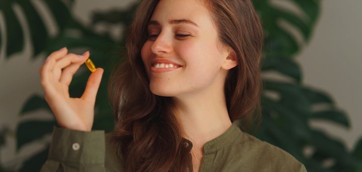Portrait of young woman holding pill, green background.