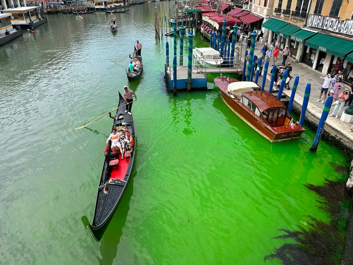 Une tache verte lumineuse est vue dans le Grand Canal le long d'un talus bordé de restaurants, à Venise, en Italie. 