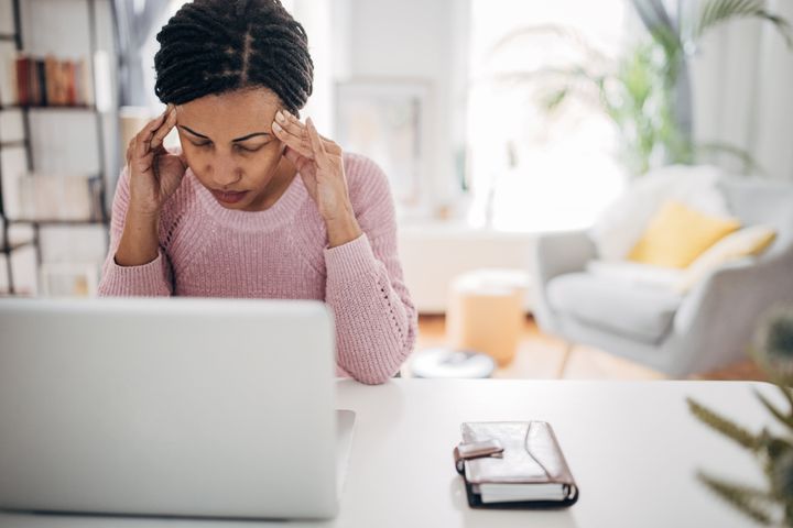 One woman, black woman having a headache while working on laptop in her home office.