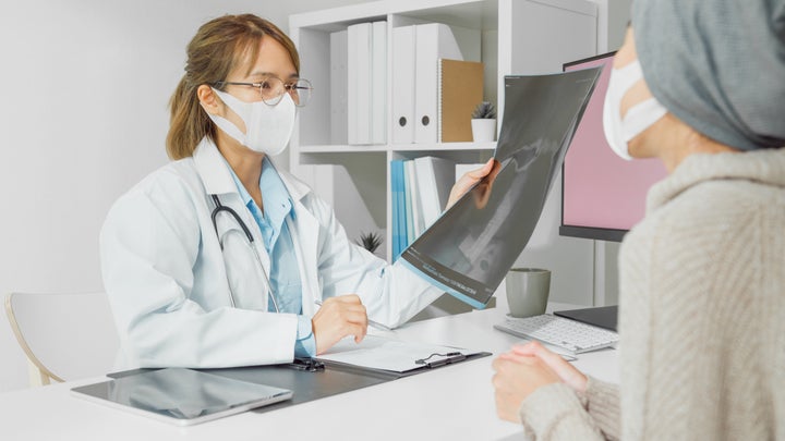 Young Asian woman doctors wear protective mask medical results during consultation with female patient sick with cancer in health clinic. Medical health care concept.