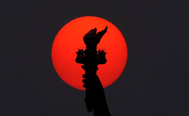 The sun is shrouded as it sets behind the Statue of Liberty in a hazy sky caused by smoke drifting into the Northeast of the U.S. from wildfires in Canada on May 22 in New York City.