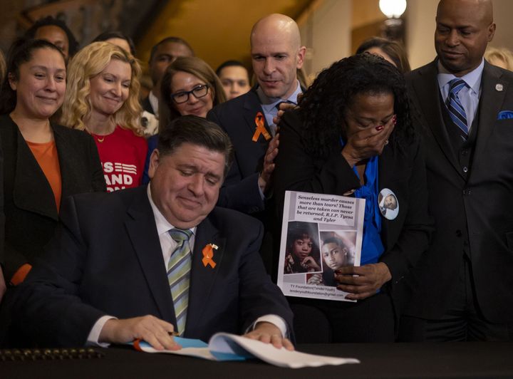 Illinois Gov. J.B. Pritzker (D) signs comprehensive legislation to ban military-style firearms on Jan. 10, 2023, while state Rep. Bob Morgan, one of the bill's authors, looks on.
