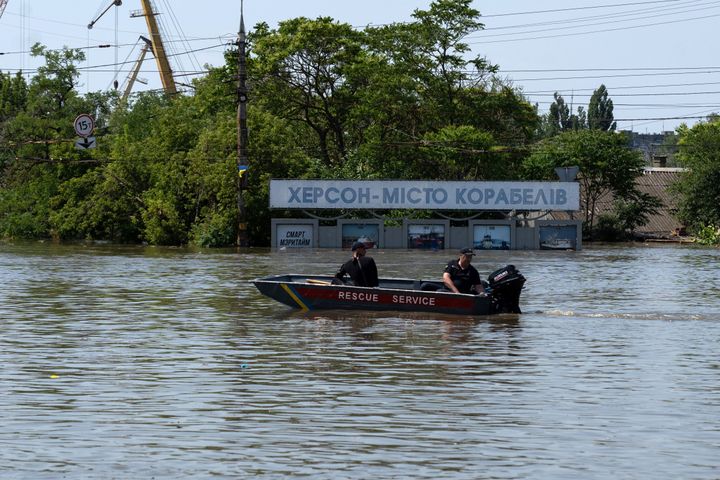 Ukrainian security sails by a placard reading "Kherson is a city of shipbuilders" on June 7, 2023 in a flooded area.