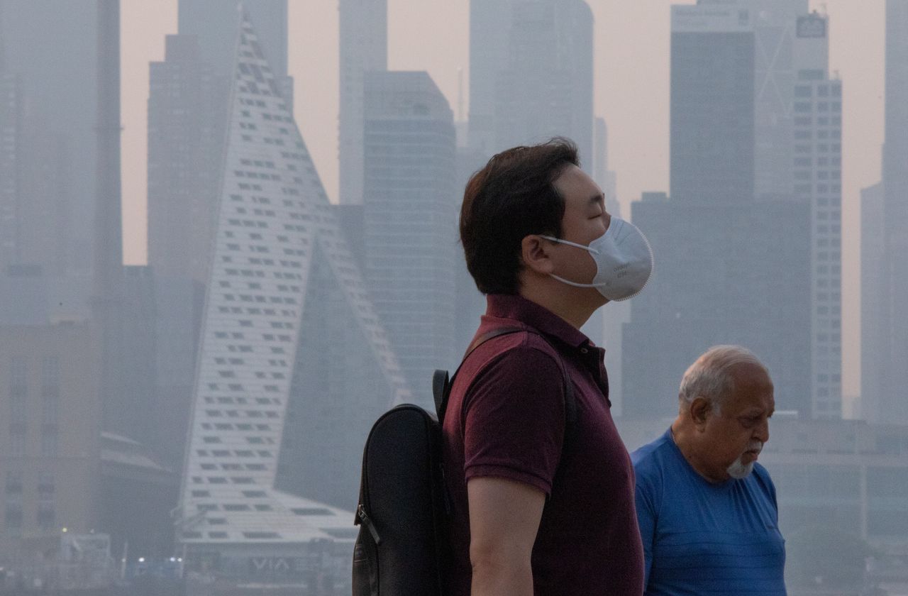 A man wears a face mask as smoke continues to cloud the sun as it rises behind the skyline of Manhattan in New York City on Wednesday as seen from Weehawken, New Jersey.
