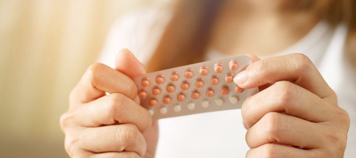 Woman hands opening birth control pills in hand.