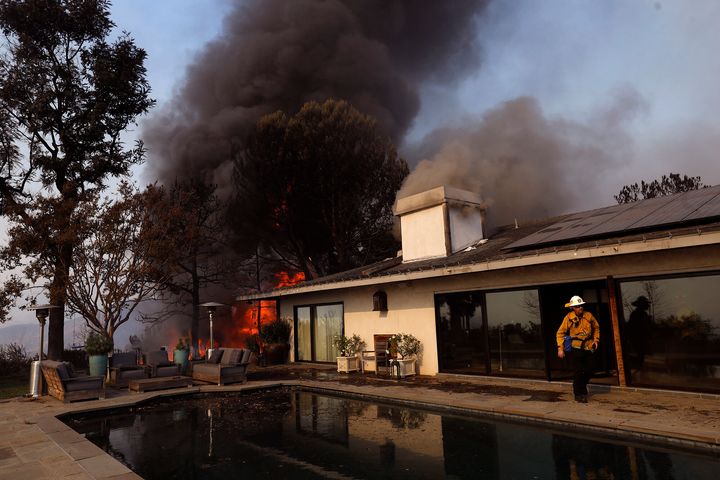A firefighter walks near a swimming pool as a Los Angeles home in the Bel-Air neighborhood is in flames from the Skirball fire on Dec. 6, 2017.