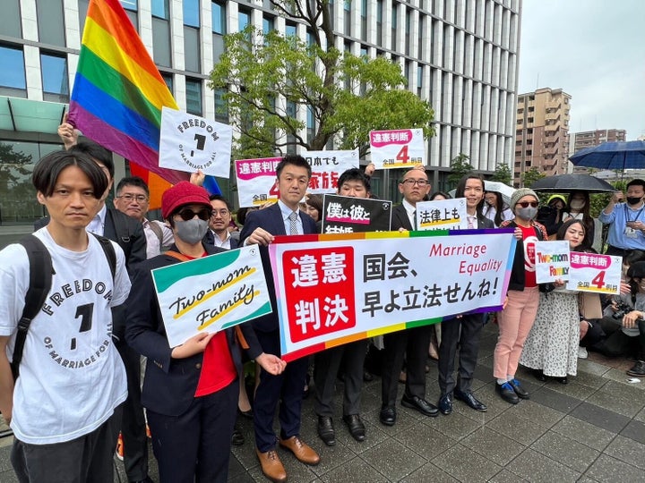 写真説明・判決後、原告と弁護団は 福岡地裁の前で「違憲判決」「国会、早よせんね!」と書かれた旗を掲げた