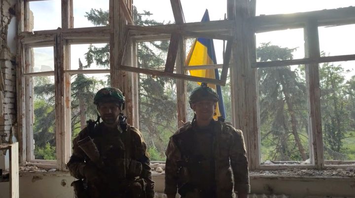 Soldiers stand in front of a Ukrainian flag at a building, during an operation that claims to liberate the first village amid a counteroffensive.
