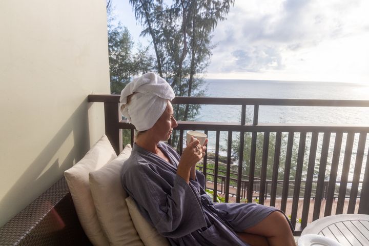 Sunrise, morning light, she wakes up with a coffee and enjoy the view from her hotel room. She wears comfortable hotel accessories such as bathrobe and towel on her head