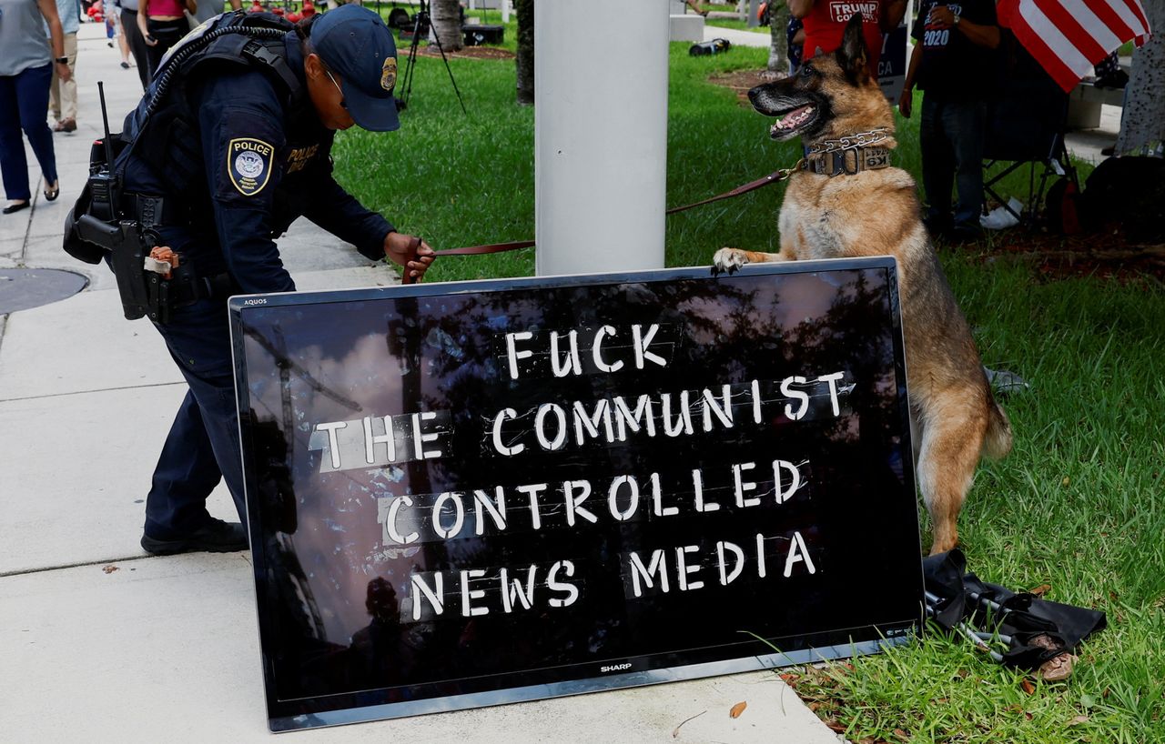 A police officer and a police dog are seen next to a sign reading "Fuck the Communist-Controlled News Media." Officers removed the sign from a post near the Wilkie D. Ferguson Jr. courthouse on the morning of June 13.