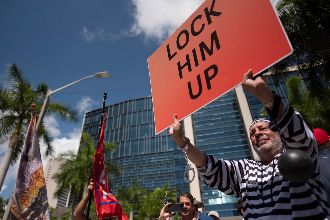 Demonstrators for and against Trump gather outside the courthouse. One holds a sign that reads "Lock Him Up."