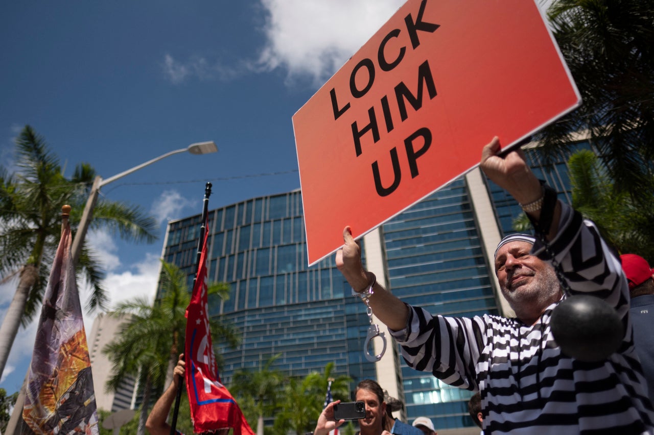 Demonstrators for and against Trump gather outside the courthouse. One holds a sign that reads "Lock Him Up."