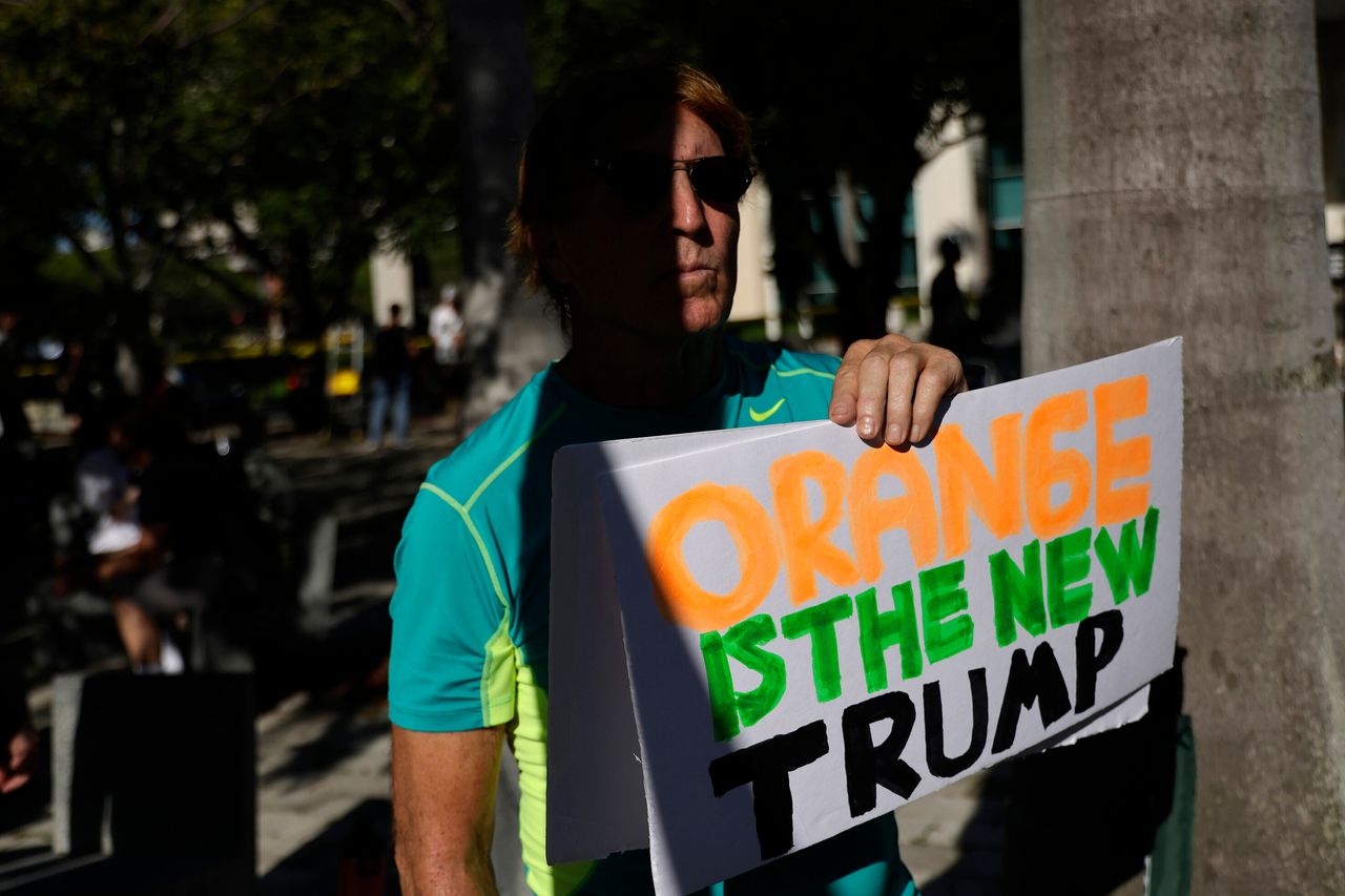 A man holds a sign outside the courthouse reading "Orange Is the New Trump."