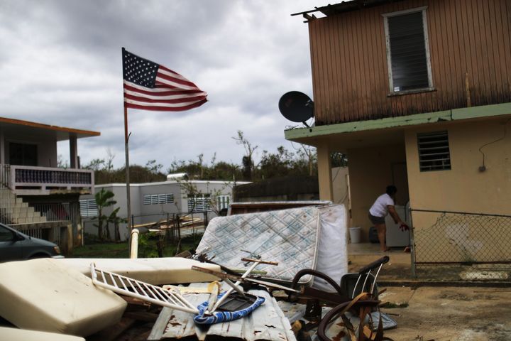 A woman stands outside of her hurricane-damaged home decorated with an American flag on Oct. 15, 2017, in Dorado, Puerto Rico.