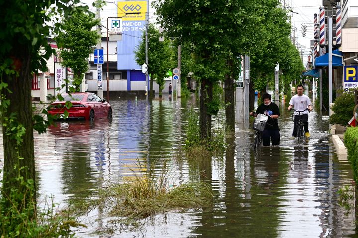 冠水した道路を自転車で移動する人たち＝6月3日午前、埼玉県越谷市