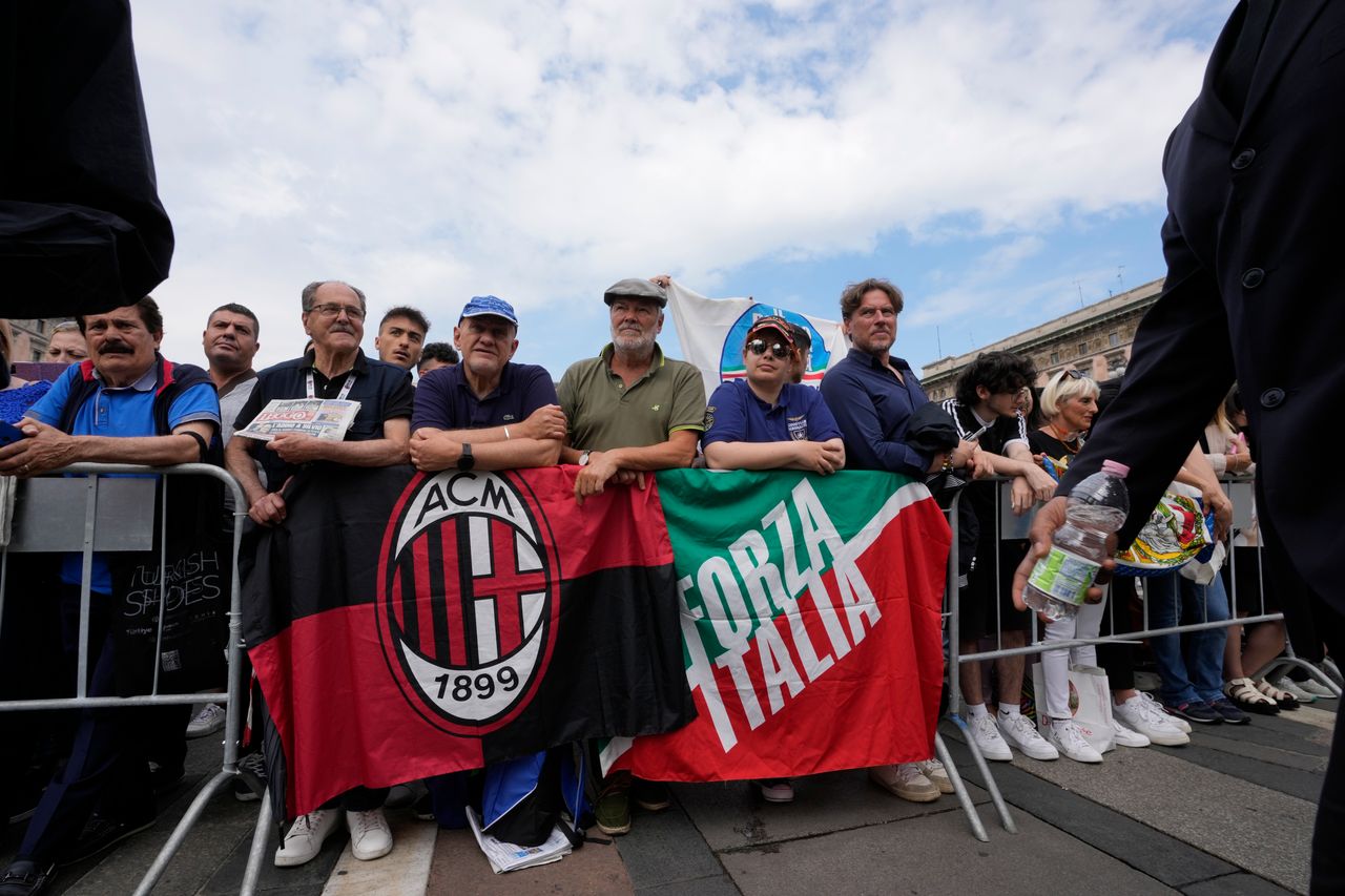 Άνθρωποι με σημαίες της Μίλαν και του κόμματος Forza Italia, που δημιουργήθηκε από τον μεγιστάνα των μέσων ενημέρωσης και πρώην πρωθυπουργό της Ιταλίας Σίλβιο Μπερλουσκόνι το 1994, περιμένουν μπροστά από τον γοτθικό καθεδρικό ναό του Μιλάνου πριν από την κηδεία του Μπερλουσκόνι, Βόρεια Ιταλία, Τετάρτη 14 Ιουνίου 2023.