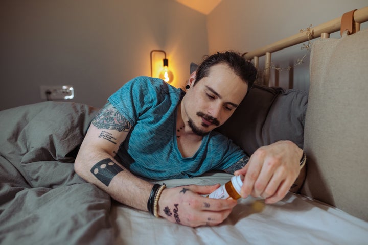 Photo of a man lying in bed and holding a pill bottle. 