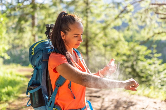 A woman applies insect repellent spray to her hands during hiking.