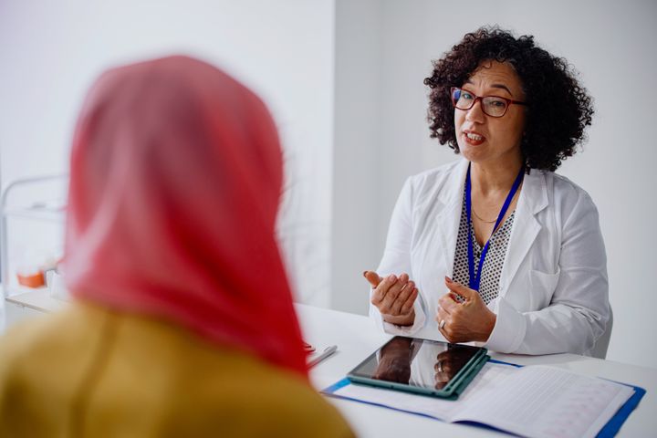 A Muslim woman sits across from her female doctor as she talks with her about cervical cancer