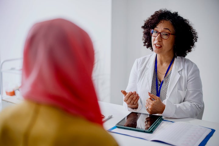 A Muslim woman sits across from her female doctor as she talks with her about cervical cancer