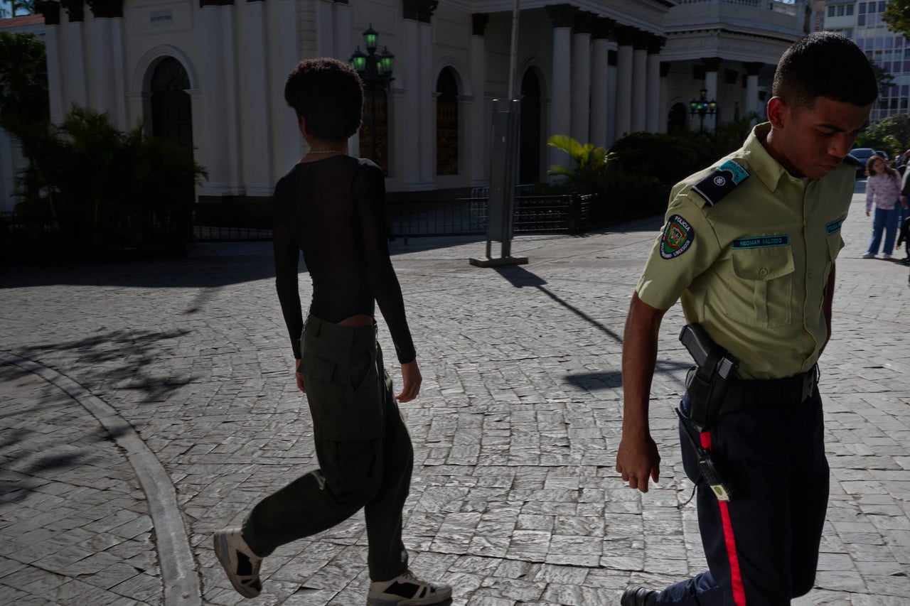 A model and trans activist named Carli (left) participates in House of Fantasy’s shoot for a trans rights video campaign in Caracas. A police officer walks by after warning about not recording in front of a legislative building.