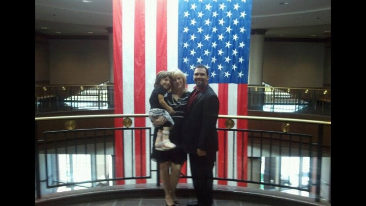 Michael, Kristine and Natalia Barnett stand in front of a flag in a family photo.