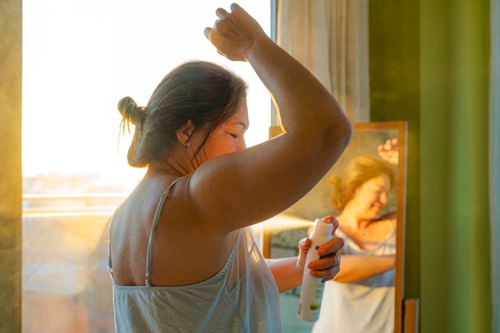 Portrait of mature woman applying deodorant on underarm in front of a mirror during morning time. 