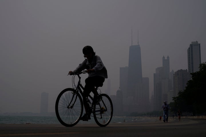 A person rides a bicycle along the shore of Lake Michigan as the downtown skyline is blanketed in haze from Canadian wildfires June 27, 2023, in Chicago.