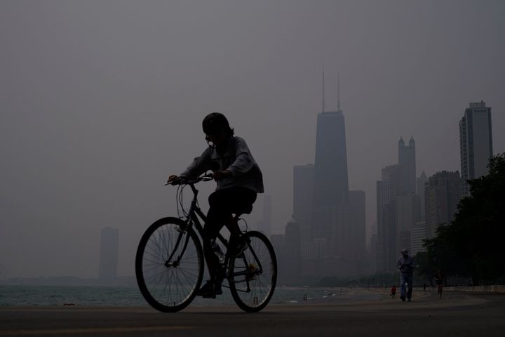 A person rides a bicycle along the shore of Lake Michigan as the downtown skyline is blanketed in haze from Canadian wildfires June 27, 2023, in Chicago. 