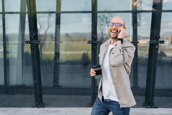 Handsome young man talking on the phone in front of a corporate building and drinking coffee outdoors.