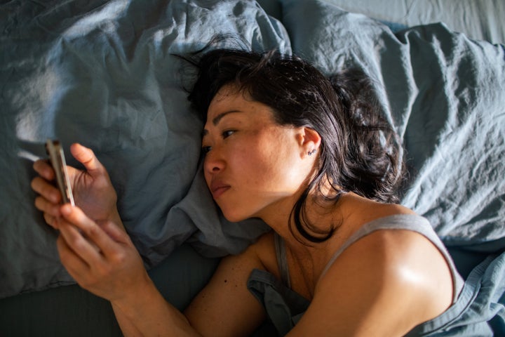 Close up of a Young Japanese woman using a smart phone while lying down in a bed