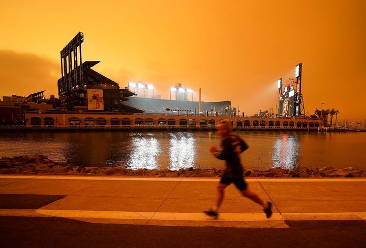 FILE - A jogger runs along McCovey Cove outside Oracle Park in San Francisco, under darkened skies from wildfire smoke on Sept. 9, 2020. As Earth's climate continues to change from heat-trapping gases spewed into the air, ever fewer people are out of reach from the billowing and deadly fingers of wildfire smoke, scientists say. (AP Photo/Tony Avelar, File)