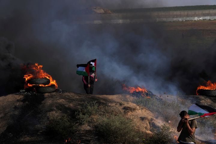 Palestinian demonstrators wave their national flags while others burn tires during a protest against an Israeli military raid in the West Bank city of Jenin, along the border fence with Israel, east of Gaza City, Monday, July 3, 2023. (AP Photo/Adel Hana)