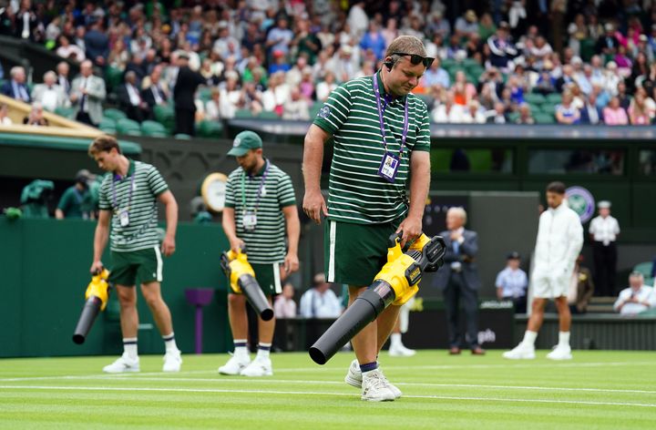 Ground staff use leaf blowers to attempt to dry the grass during a rain delay on centre court on day one of the 2023 Wimbledon Championships at the All England Lawn Tennis and Croquet Club in Wimbledon. 
