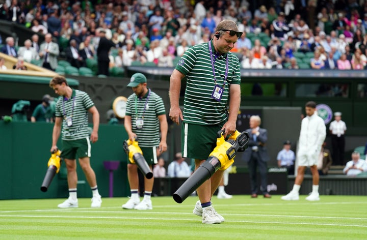 Ground staff use leaf blowers to attempt to dry the grass during a rain delay on centre court on day one of the 2023 Wimbledon Championships at the All England Lawn Tennis and Croquet Club in Wimbledon. 