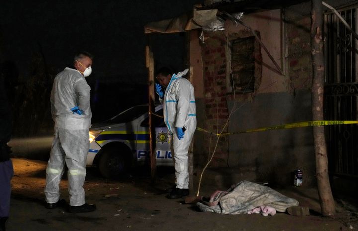 Police stand near a covered body in the Angelo settlement in Boksburg, South Africa, Thursday, July 6, 2023. Police said over a dozen people, including children, have died from a toxic gas leak in the informal settlement. (AP Photo/Themba Hadebe)