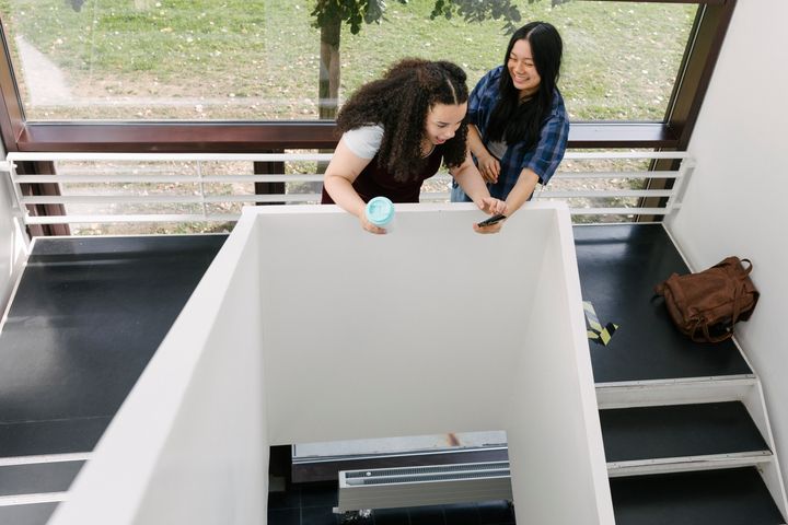 Twostudents laughing while looking at a smartphone and hanging out in a stairwell.