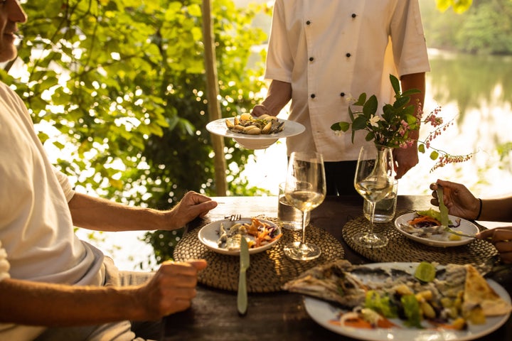 Waiter serving food to a man and woman in restaurant on patio by the river.